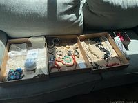 Three trays on sofa containing jewelry, linens, trinket jar