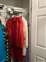 Closet view with multiple garments including red suit, cream top, purple dress, plaid coat
