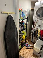 Overall view of closet with ironing board, shelving, stacked cleaners, brooms and mop