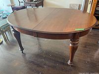 Full view of oval dining table showing dark wood finish, turned legs, one brass caster visible