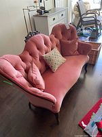 Front view showing pink velvet settee with three cushions, tufted back and carved wood frame
