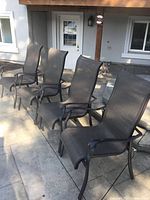 Four matching aluminum and mesh patio chairs lined up on stone patio