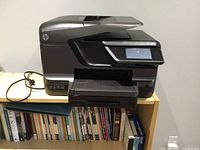 Front view of HP OfficeJet Pro 8600 Plus printer on shelf with power cord visible