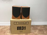 Front view of both Mission M31 speakers on top of original box, showing grilles and wood finish