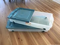 Both Rubbermaid containers stacked, showing clear bodies, teal lids, wheels