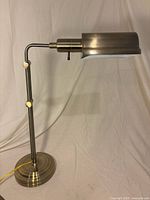 Front view of brushed brass adjustable banker-style desk lamp showing shade, arm, base, and cord