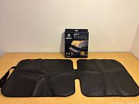 Front view of unfolded black Diono Grip It car seat protector mat with packaging box