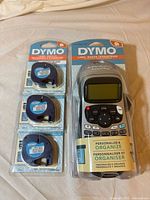 Front view of sealed DYMO LetraTag 100H label maker and three sealed tape refills