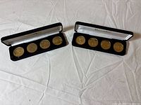 Two velvet cases open, each showing four gold-tone coins