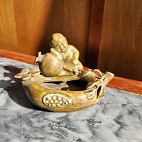 Oblique view of glazed ceramic dish showing baby figure on pomegranate and seed relief