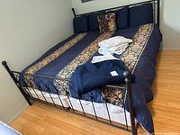 Full view of bed dressed with blue and gold bedding, pillows, fleece blanket