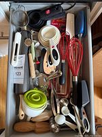 Top view of drawer with assorted utensils showing measuring cups, spoons, whisks, spatulas, strainers, thermometer package and other tools