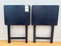 Two navy blue folding TV trays shown folded flat against wall