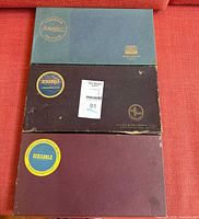 Three stacked Scrabble boxed sets showing front lids and logos