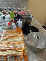 Countertop view showing angel food pan, mixing bowls, spatulas, squeeze bottles, measuring cylinder, silicone mold, striped textile