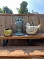 Three garden items on bench: fish planter, bird finial statue, bird planter