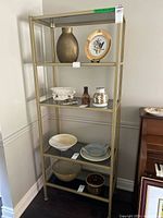 Full view of gold tone metal shelving unit with four glass shelves