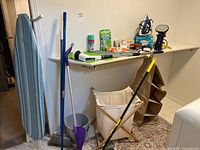 Wide shot of lot showing ironing board, hamper, cleaning tools, shelf with small appliances and supplies