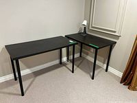 Two black desks arranged in L-shape with lamp on smaller desk