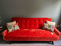 Full view of rusty orange velvet futon with two accent pillows