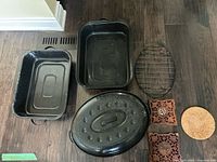 Full lot showing two rectangular roasting pans, oval lid, metal rack, two wooden trivets, cork trivet