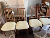 Front view of four teak dining chairs showing slat backs and fabric seats