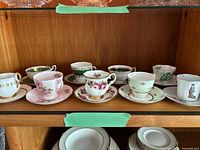 Eight of the nine teacup sets on cabinet shelf