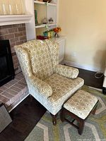 Wingback chair beside fireplace showing upholstery pattern and ottoman front