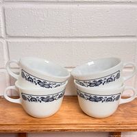 Stacked view of four white Pyrex mugs showing blue Onion pattern and handles