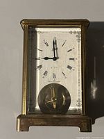 Front view of antique brass mantel clock showing clock face with Roman numerals, Schatz brand name, and 8 day indication, along with visible pendulum.