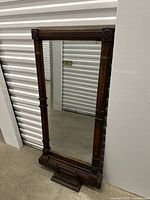 Full view of the rectangular antique mirror in a dark wood frame with carved decorations around the frame.
