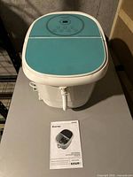 Front view of white and teal Costway foot spa with manual placed in front on a table.
