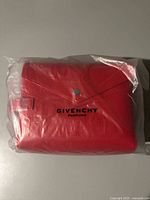 Front view of the red Givenchy perfume travel bag in clear plastic packaging, showing embossed logo and snap button closure.