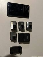 Top down photo showing all items together on table: 4 GoPro cameras, Sony charger, Samsung tablet.