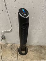 Full view of black Honeywell tower fan standing on concrete floor with power cord visible.