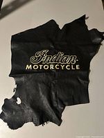 Photo of a black leather piece with embroidered Indian Motorcycle logo in beige stitched thread.