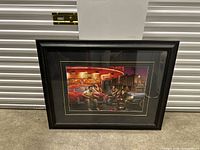Photo of large framed artwork depicting a retro night scene with people and vintage cars, seen against a storage door.