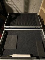 Interior photo of one protective travel case showing black foam padding lining the inside for protective cushioning. Contents include a white power strip.