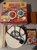 Taiko no Tatsujin game box, drum controller, and drumsticks arranged on a surface