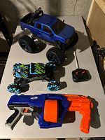 Photo showing all three items: blue RC truck, remote control stunt car, and toy blaster gun.