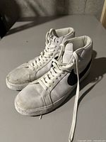 Pair of white Nike high-top sneakers size 10.5 with black swoosh logos on a gray surface showing dirt and wear marks on the fabric and soles.