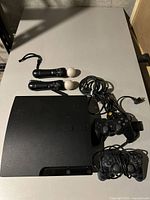 Top-down view of PlayStation 3 console with two DualShock controllers and two PlayStation Move motion controllers arranged on table.