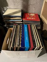 Wide view of various vinyl record albums stacked in a white box and piles showing album cover edges and spines