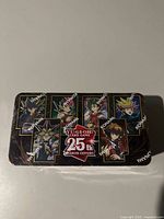 Front view of sealed tin showing characters and 25th anniversary logo.