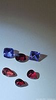 Five loose natural gemstones including two cushion-cut tanzanites, one oval sapphire, and two pear-shaped spinels.