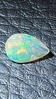 Close-up photo of pear-shaped faceted Ethiopian opal showing vibrant play of color on dark textured background.