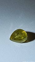 Photo of a pear cut yellow-green natural African sphene gemstone on a white background under light showing facets and some internal inclusions.
