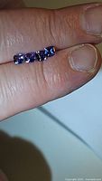 Four small cushion cut tanzanite gemstones placed on a finger showing their rich blue color and clarity.