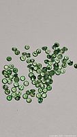 Photo showing multiple small round cut natural tsavorite garnet gemstones in bright green color scattered on a light background.