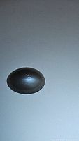 Close-up image of a single oval cabochon catseye moonstone showing reflective catseye line across the surface on a grey background.